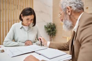 Two professionals, a middle-aged woman and an elderly man, review estate planning documents at a table in a modern office setting.